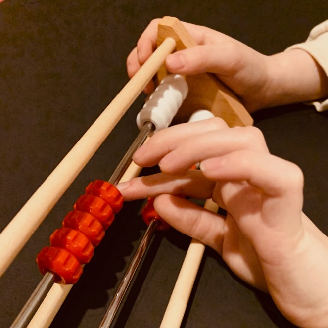 A child uses one hand to steady a Dutch counting frame called a rekenrek and slides some beads along the top row